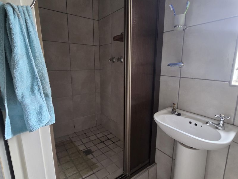 A functional bathroom featuring a pedestal basin and a shower enclosure with tiled finishes, requiring some maintenance and cosmetic updates.
