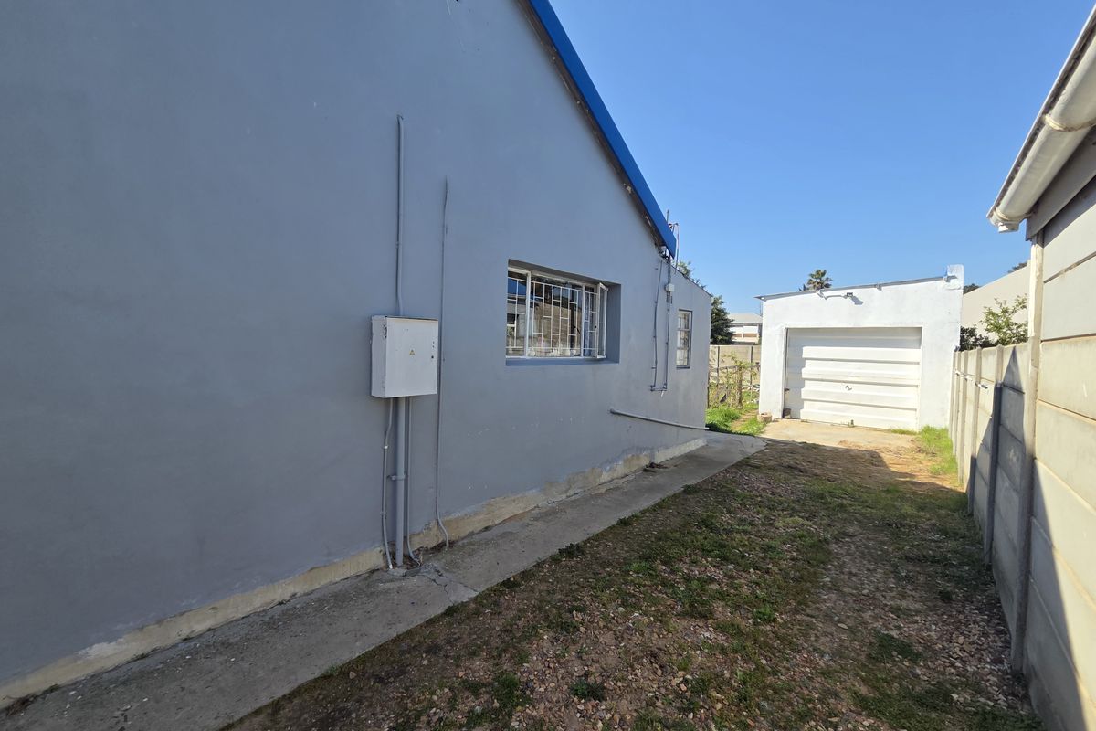 Rear exterior view of the property featuring a concrete pathway, detached garage, and boundary walling.