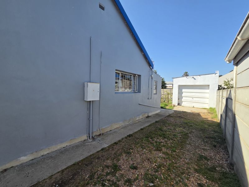 Rear exterior view of the property featuring a concrete pathway, detached garage, and boundary walling.