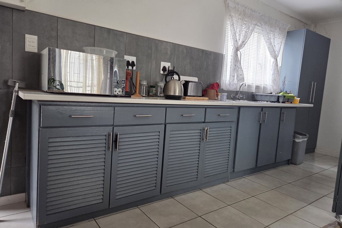 A functional kitchen featuring grey louvered cabinetry, a tiled backsplash, and neutral floor tiles, providing a practical workspace with ample storage.