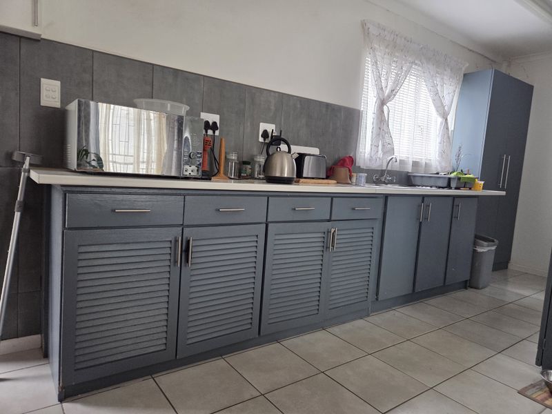 A functional kitchen featuring grey louvered cabinetry, a tiled backsplash, and neutral floor tiles, providing a practical workspace with ample storage.