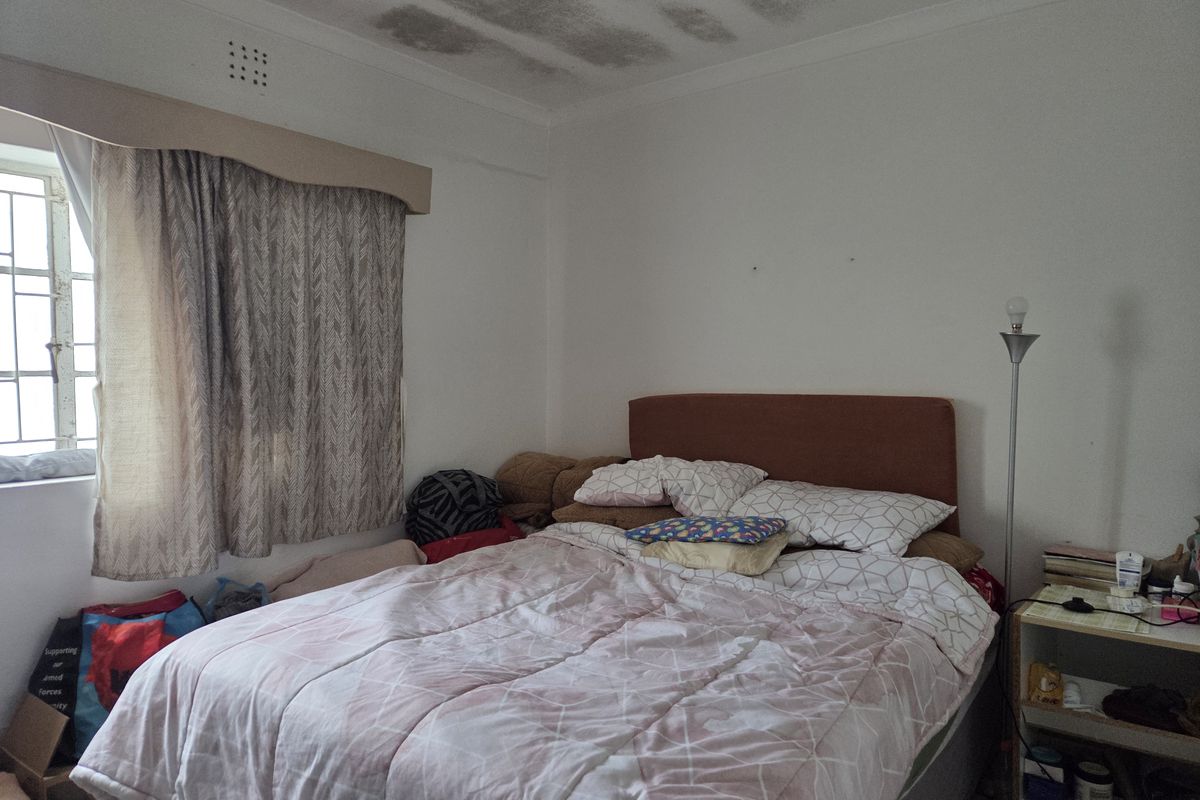 A bedroom featuring security bars on the window and a ventilation grille, currently showing significant water staining on the ceiling.