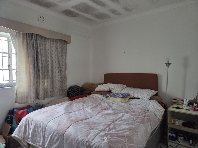 A bedroom featuring security bars on the window and a ventilation grille, currently showing significant water staining on the ceiling.