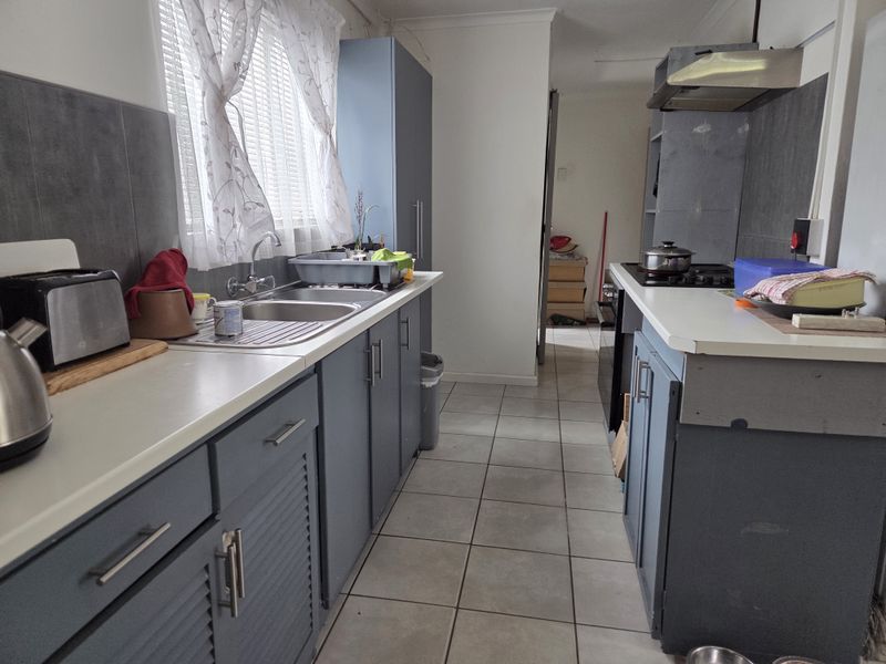 Functional kitchen featuring blue built-in cabinetry, tiled flooring, a stainless steel sink, and a gas hob with an extractor fan.