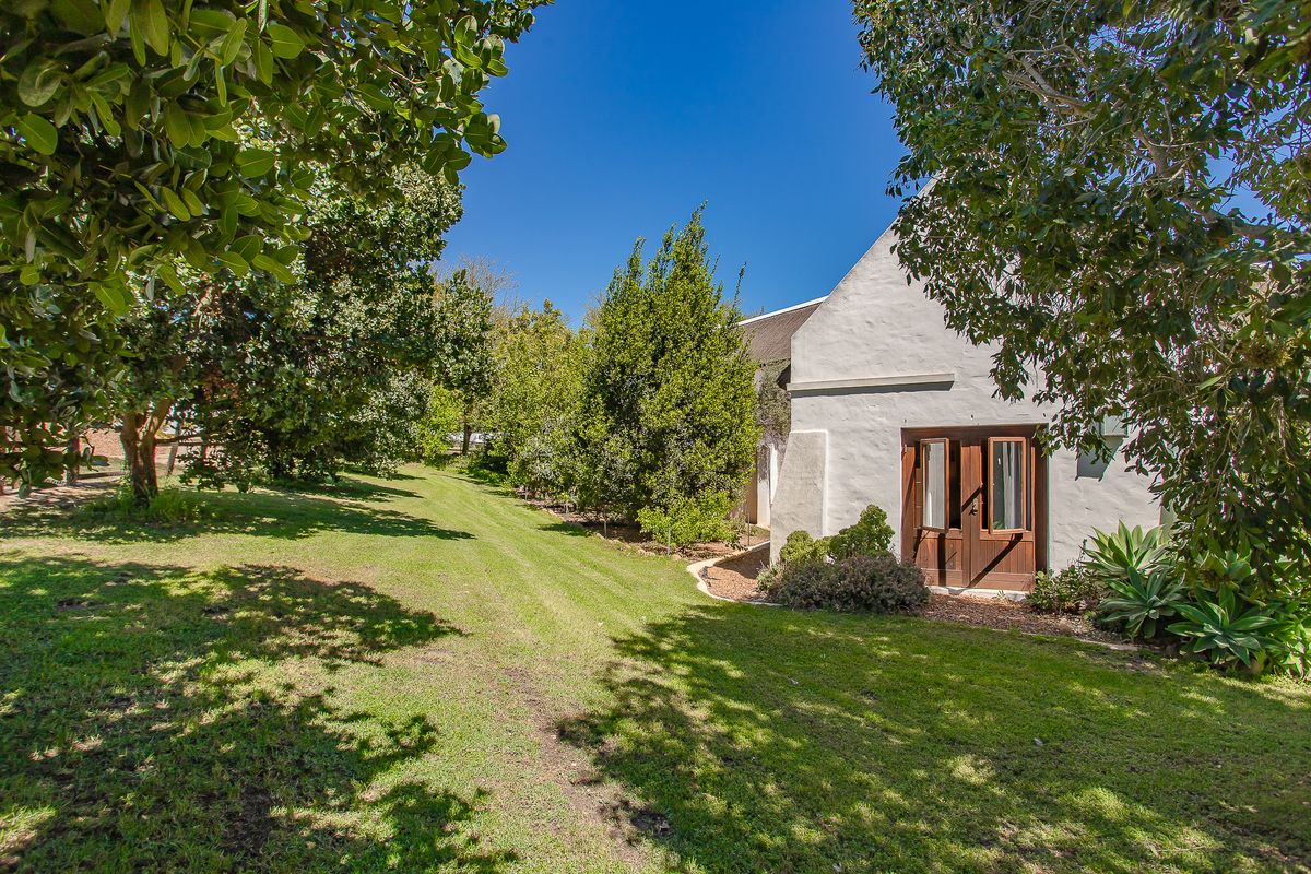 A view of the rear garden featuring a well-maintained lawn, mature trees, and access to the home through timber-framed double doors.