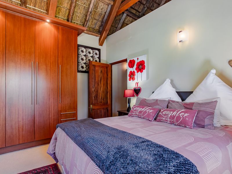 A cozy bedroom featuring a high thatched ceiling with exposed timber rafters and extensive built-in wooden cupboards.