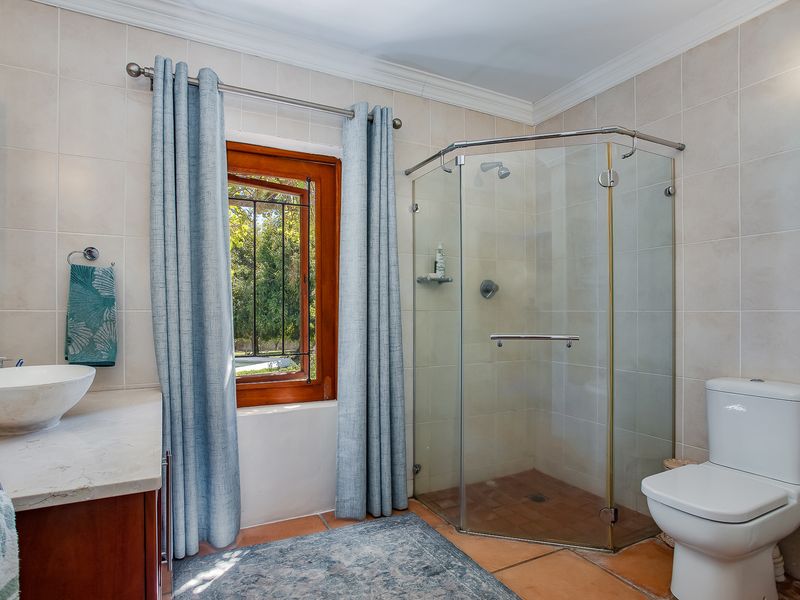 A well-maintained bathroom featuring a corner glass shower, vessel sink on a stone vanity, and classic tiled finishes with a timber-framed window.