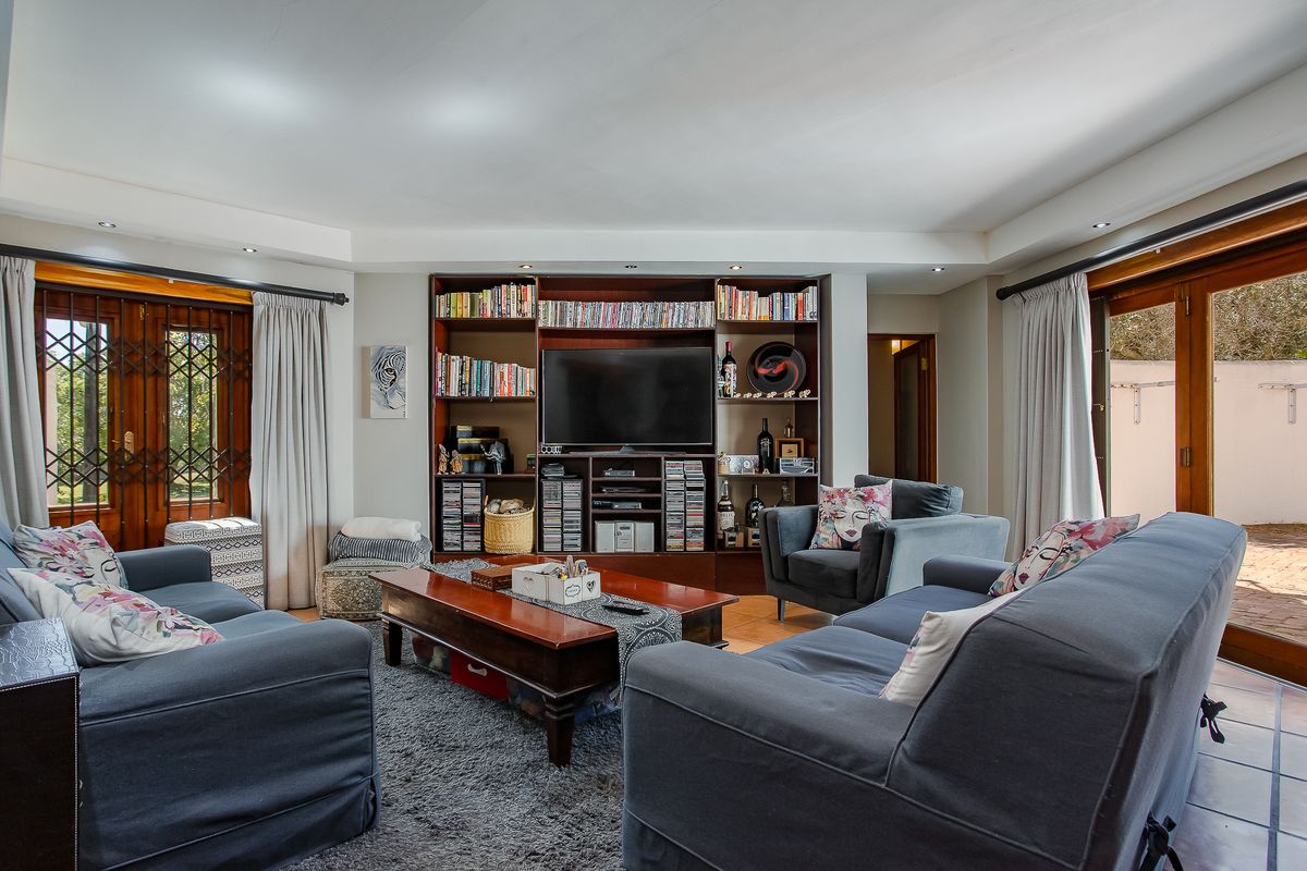 A comfortable living room featuring a large built-in shelving unit, recessed lighting, and direct access to outdoor areas through wooden framed glass doors.