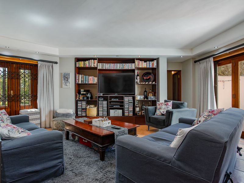 A comfortable living room featuring a large built-in shelving unit, recessed lighting, and direct access to outdoor areas through wooden framed glass doors.