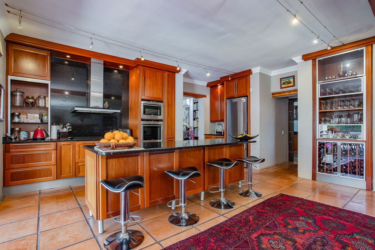 Spacious kitchen featuring warm wooden cabinetry, granite countertops, a central island with breakfast bar, and integrated appliances including a built-in oven and wine storage.