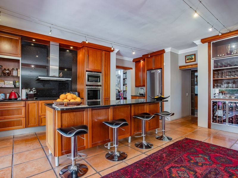 Spacious kitchen featuring warm wooden cabinetry, granite countertops, a central island with breakfast bar, and integrated appliances including a built-in oven and wine storage.