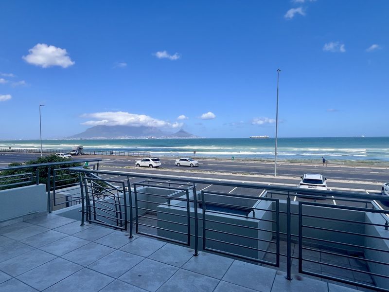 A spacious balcony featuring tiled flooring and a metal balustrade, offering panoramic views of the ocean and Table Mountain.