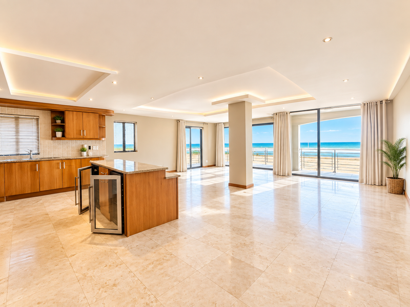 Spacious open-plan living and kitchen area featuring tiled floors, modern cabinetry, and expansive sliding doors opening to a scenic ocean view.