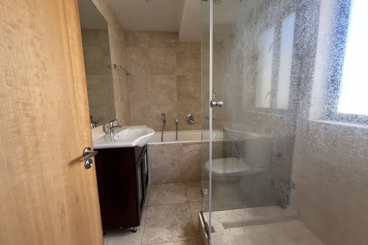 A functional bathroom featuring a vanity basin, bathtub, separate shower enclosure with glass screen, and neutral stone-style wall and floor tiling.