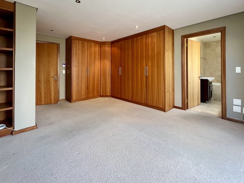 Spacious bedroom featuring extensive built-in wooden cabinetry, integrated shelving, neutral carpeting, and direct access to an en-suite bathroom.