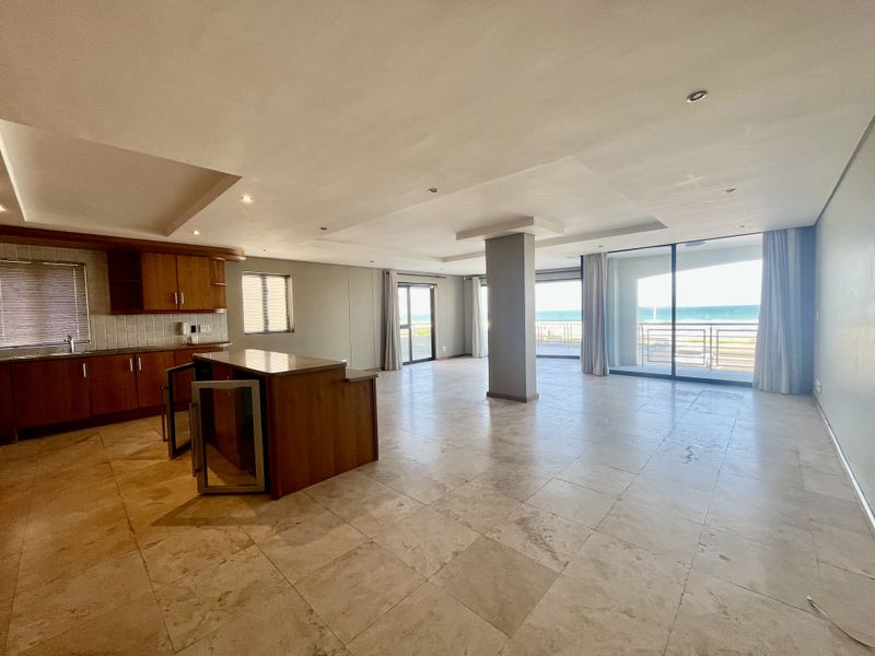 Spacious open-plan living and kitchen area featuring stone tile flooring, built-in cabinetry, and large sliding doors opening to a scenic ocean view.