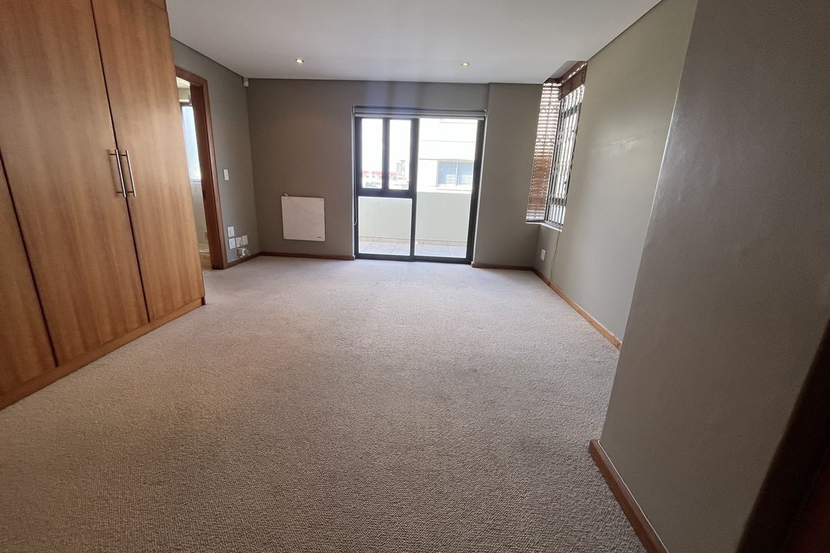Spacious bedroom featuring neutral carpeting, built-in wooden cupboards, recessed lighting, and a sliding glass door providing access to a balcony.