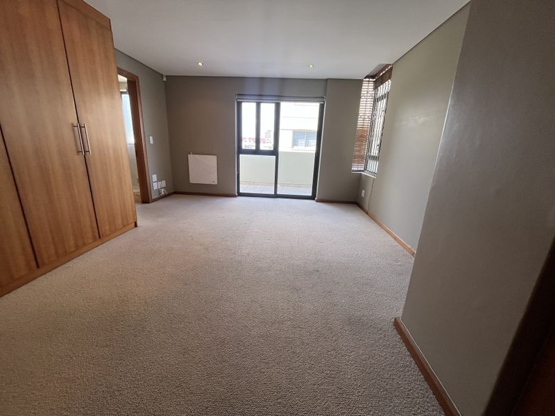 Spacious bedroom featuring neutral carpeting, built-in wooden cupboards, recessed lighting, and a sliding glass door providing access to a balcony.