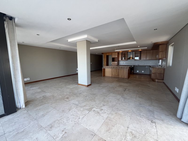 Spacious open-plan living and kitchen area featuring travertine flooring, a central structural pillar, and wooden cabinetry with integrated kitchen fixtures.