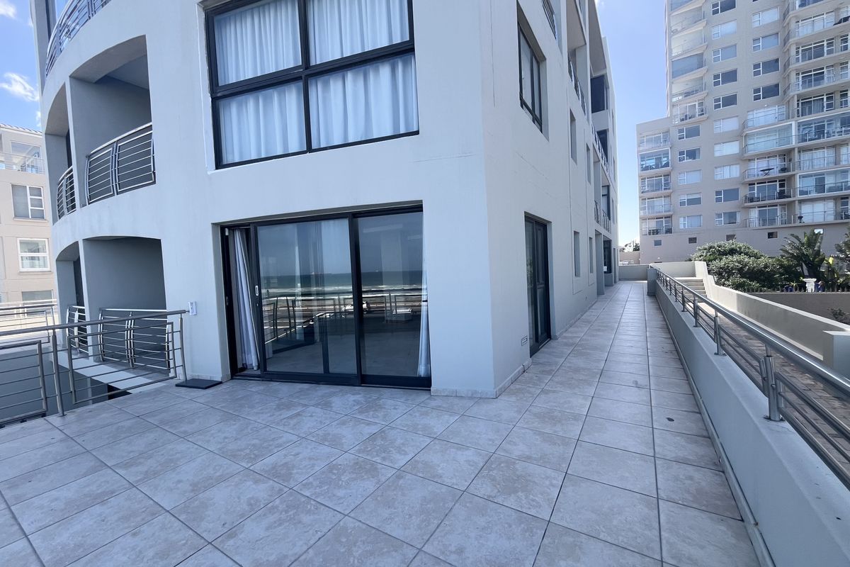 A spacious, tiled balcony area featuring modern stainless steel balustrades and large sliding glass doors providing access to the apartment interior.