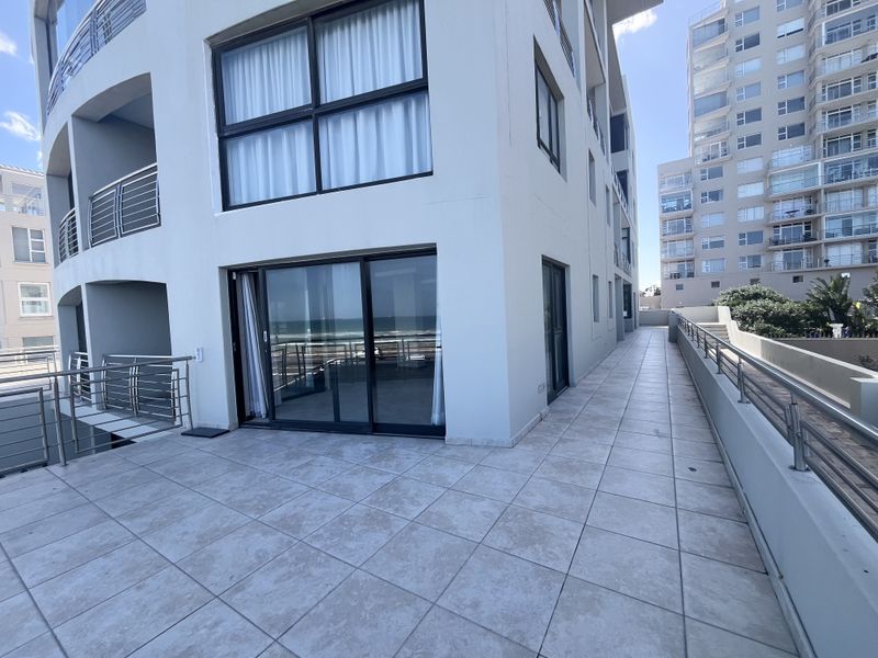 A spacious, tiled balcony area featuring modern stainless steel balustrades and large sliding glass doors providing access to the apartment interior.