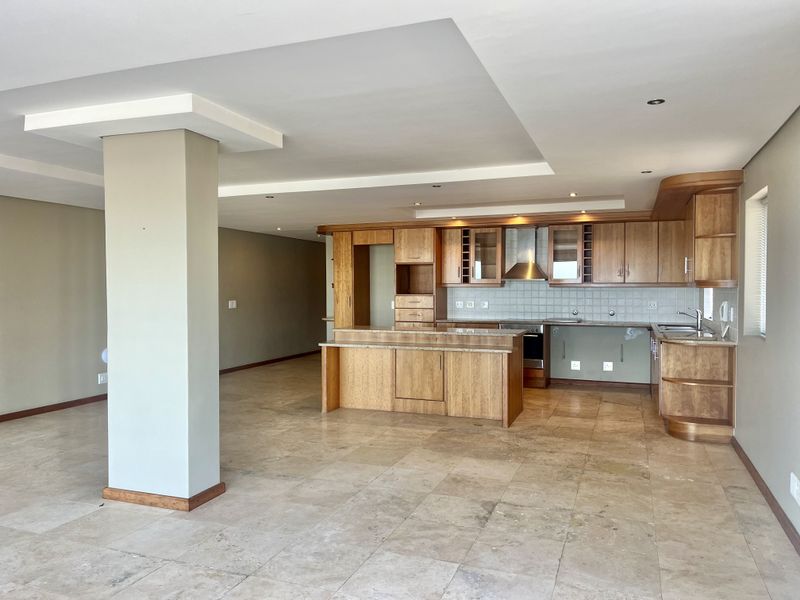 Spacious open-plan living and kitchen area featuring stone tile flooring, wooden cabinetry, granite countertops, and a modern recessed ceiling design.