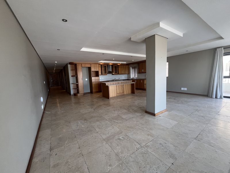 Spacious open-plan living and kitchen area featuring stone tile flooring, wooden cabinetry, a central kitchen island, and modern recessed ceiling lighting.