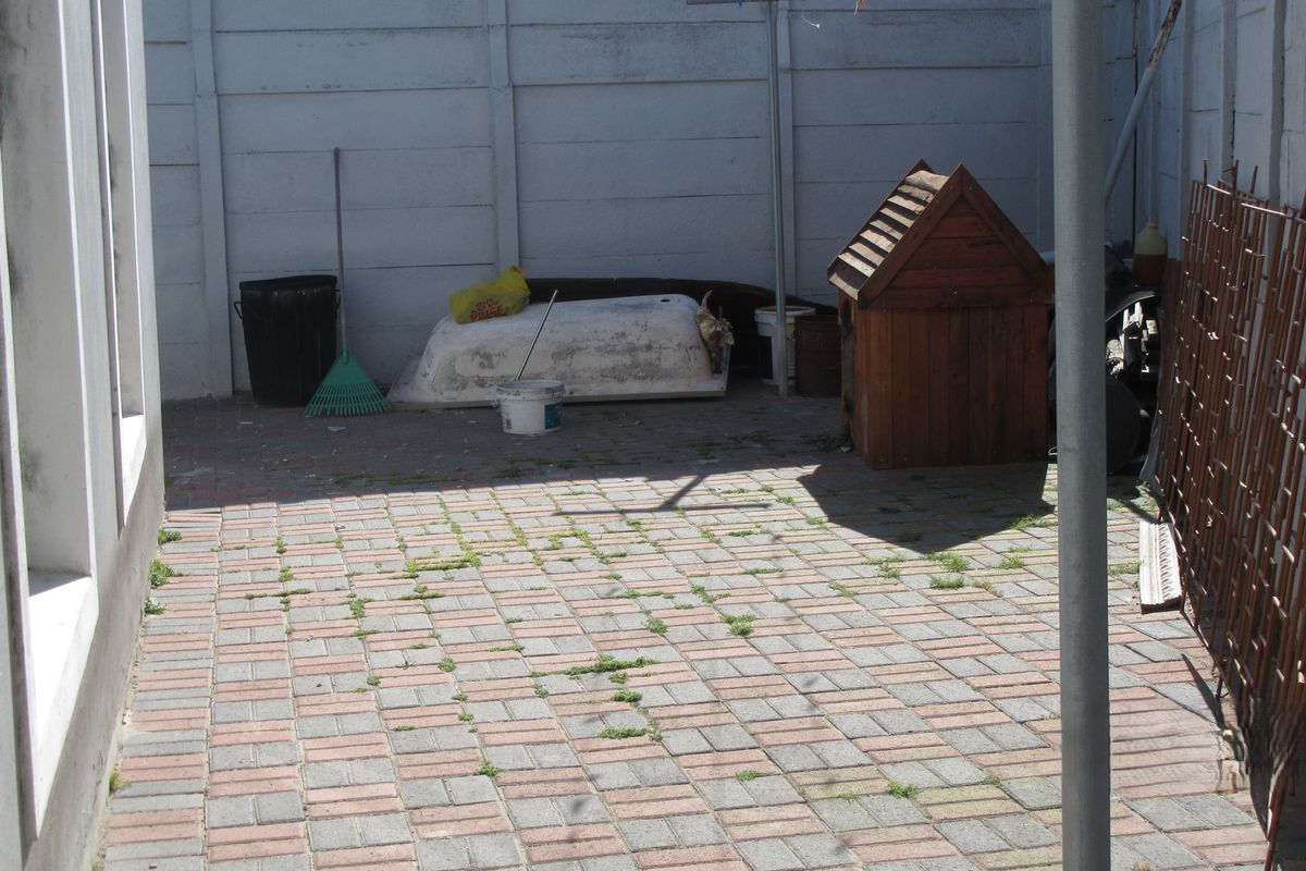 A paved rear courtyard area enclosed by precast concrete walls, requiring maintenance and cleaning.