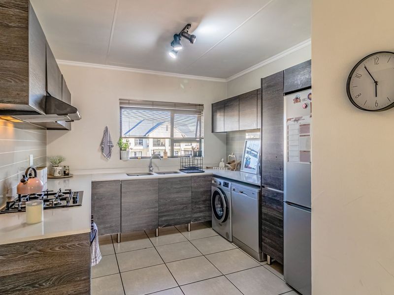 Modern kitchen featuring dark wood-grain cabinetry, gas hob, extractor fan, double sink, and integrated space for laundry appliances with tiled flooring.
