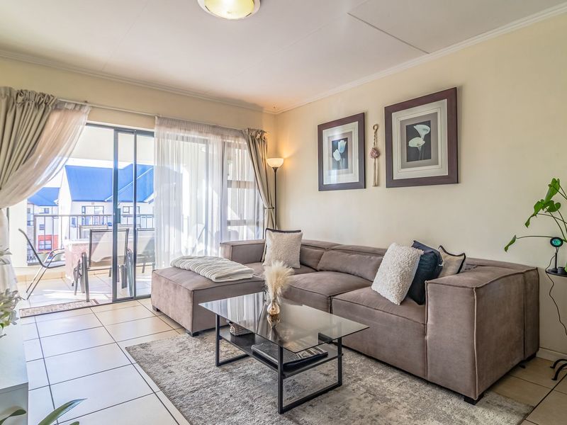 A bright living room featuring tiled flooring and large sliding glass doors that provide direct access to an outdoor balcony area.