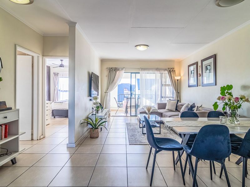 Spacious open-plan living and dining area featuring neutral tiled flooring, ample natural light, and seamless access to an outdoor balcony.
