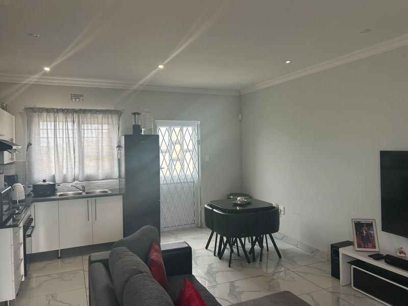 Open-plan living area featuring a modern kitchen with built-in cabinetry, tiled flooring, and direct access to the exterior via a security gate.