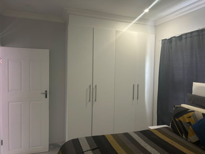 A bedroom featuring white built-in cupboards with modern handles and decorative ceiling cornice.