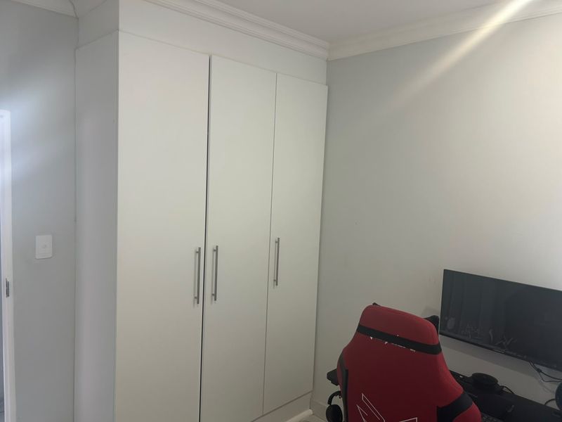 A bedroom featuring a clean, white built-in wardrobe with modern handles and decorative ceiling cornicing.