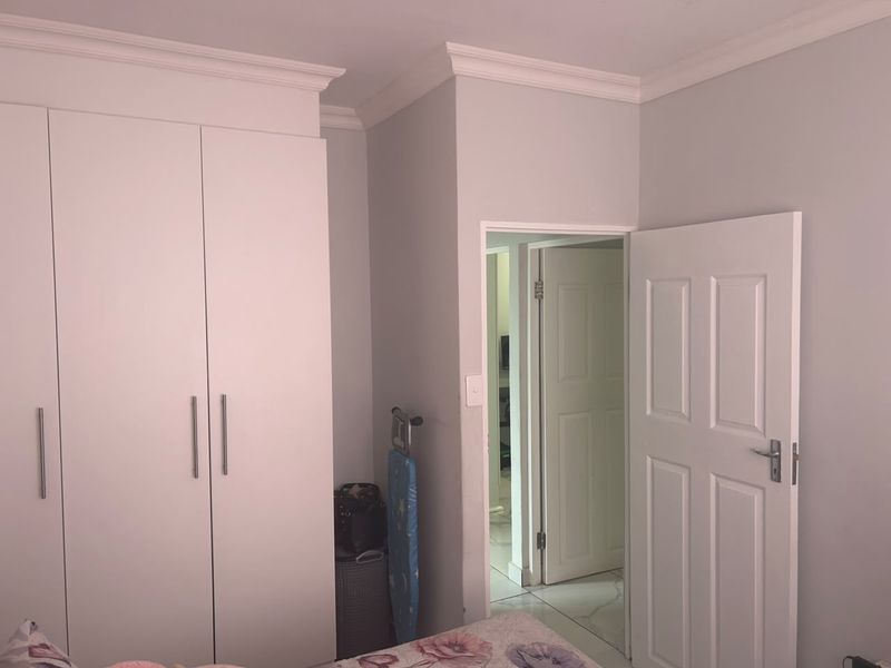 A bedroom featuring built-in cupboards with modern handles, decorative ceiling cornicing, and a classic panel door leading to an adjacent hallway.