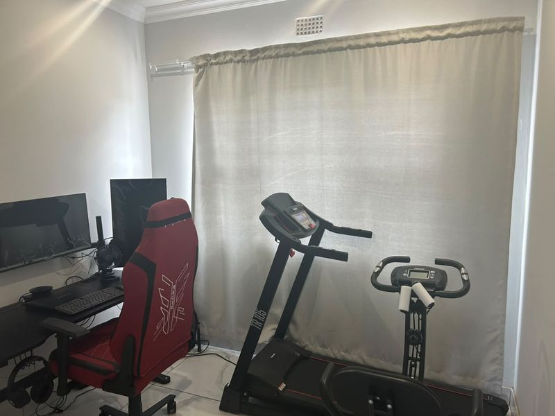 A multi-purpose room currently utilized as a home office and gym space, featuring tiled flooring and neutral wall finishes.