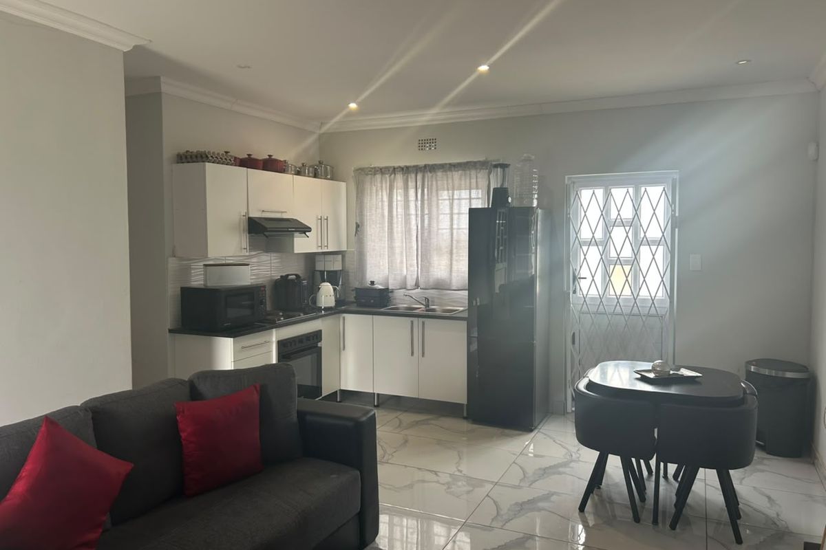 Open-plan kitchen and living area featuring modern white cabinetry, tiled flooring, and direct access to a secure exterior door.