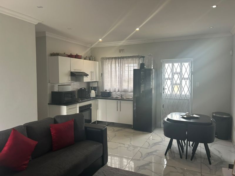 Open-plan kitchen and living area featuring modern white cabinetry, tiled flooring, and direct access to a secure exterior door.
