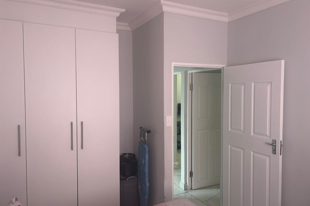 A bedroom featuring built-in cupboards, crown molding, and tiled flooring, with a doorway leading to an adjacent room.