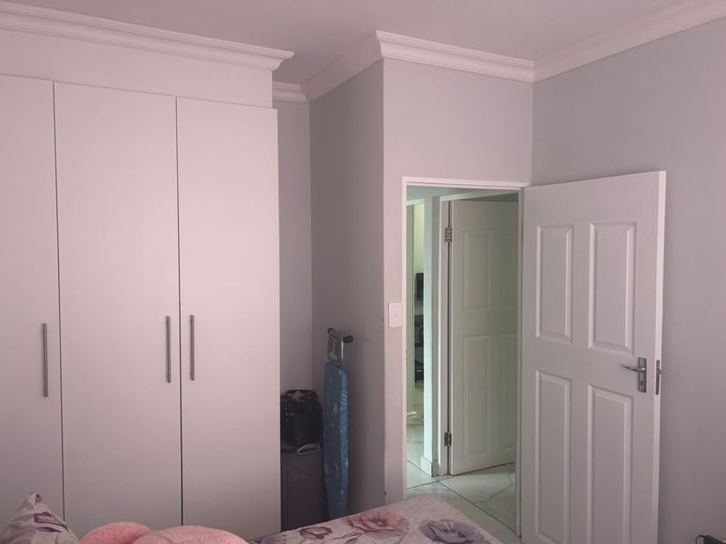 A bedroom featuring built-in cupboards, crown molding, and tiled flooring, with a doorway leading to an adjacent room.