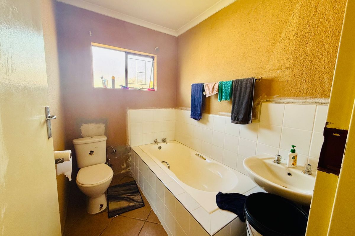 A functional bathroom featuring a built-in bathtub, pedestal basin, and toilet, requiring cosmetic updates to the wall finishes and tiling.
