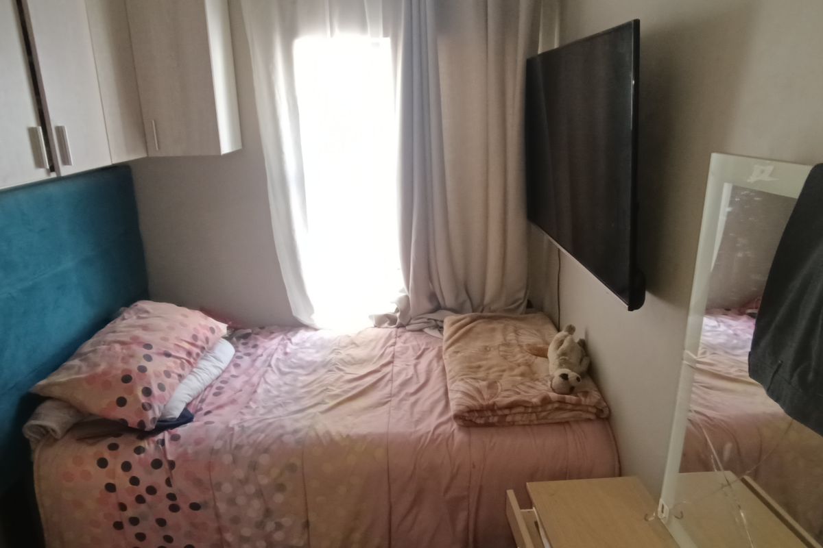 A compact bedroom featuring built-in overhead cabinetry and a wall-mounted television, providing efficient use of space.