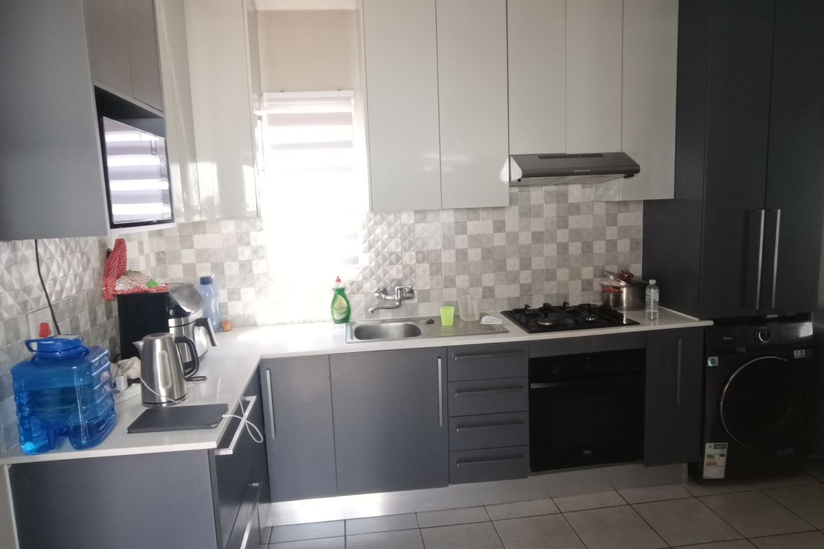 Modern kitchen featuring two-tone cabinetry, gas hob, built-in oven, extractor fan, and integrated laundry appliance with a tiled backsplash and floor.