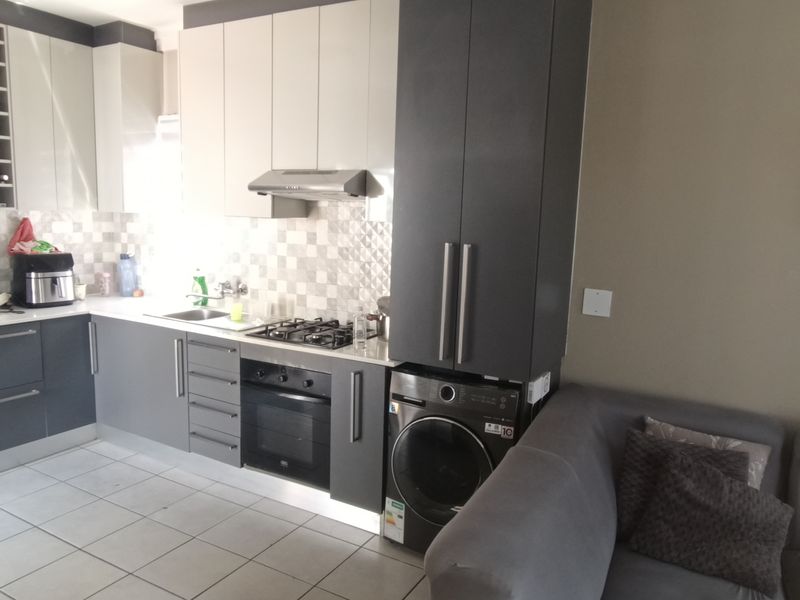 Modern open-plan kitchen featuring two-tone cabinetry, gas hob, built-in oven, and integrated laundry appliance, seamlessly connected to the living area.