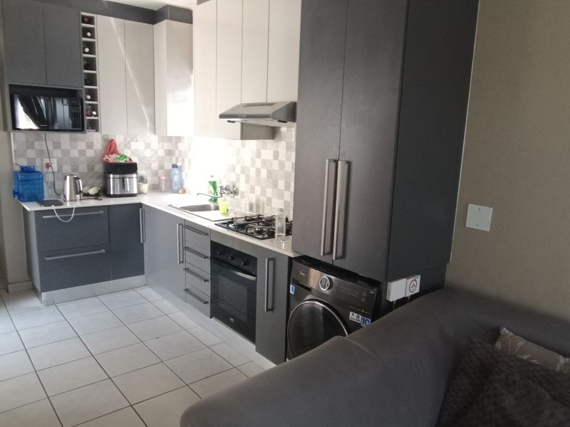 Modern open-plan kitchen featuring two-tone cabinetry, built-in oven, gas hob, and tiled flooring, seamlessly integrated into the living space.