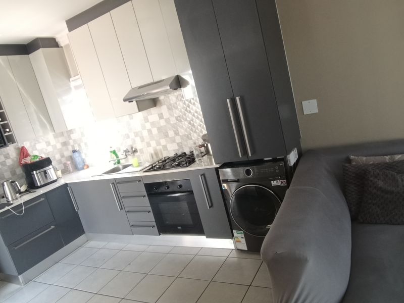 Modern open-plan kitchen featuring sleek two-tone cabinetry, gas hob, built-in oven, and integrated laundry appliance, seamlessly connected to the living area.