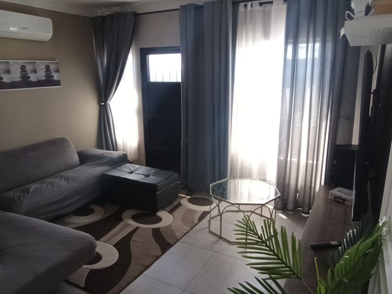 A comfortable living room featuring tiled flooring, decorative wall molding, and a wall-mounted split-system air conditioner with access to an outdoor area.