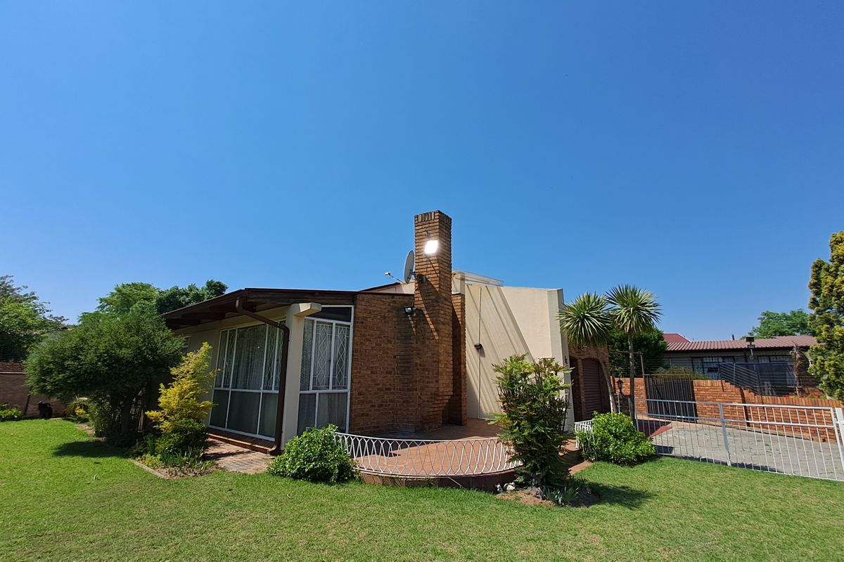 Rear view of the house featuring a brick chimney, a paved patio area, and a well-maintained garden with perimeter fencing.