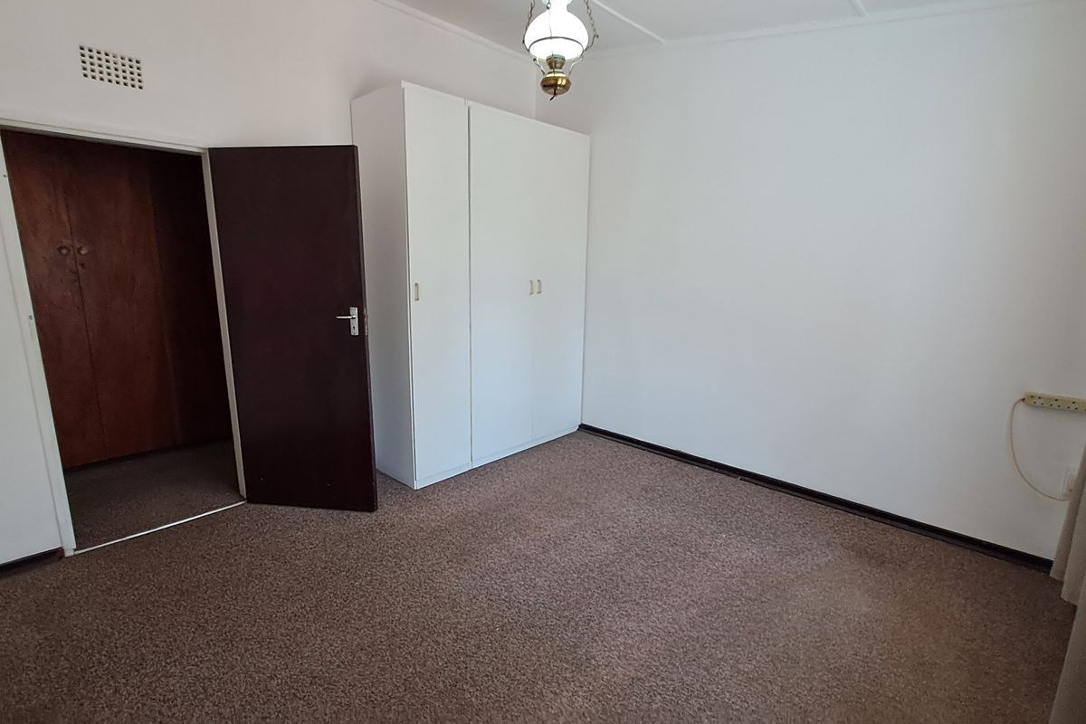 A simple, vacant bedroom featuring neutral walls, carpeted flooring, and a built-in wardrobe, offering a clean canvas for personalization.