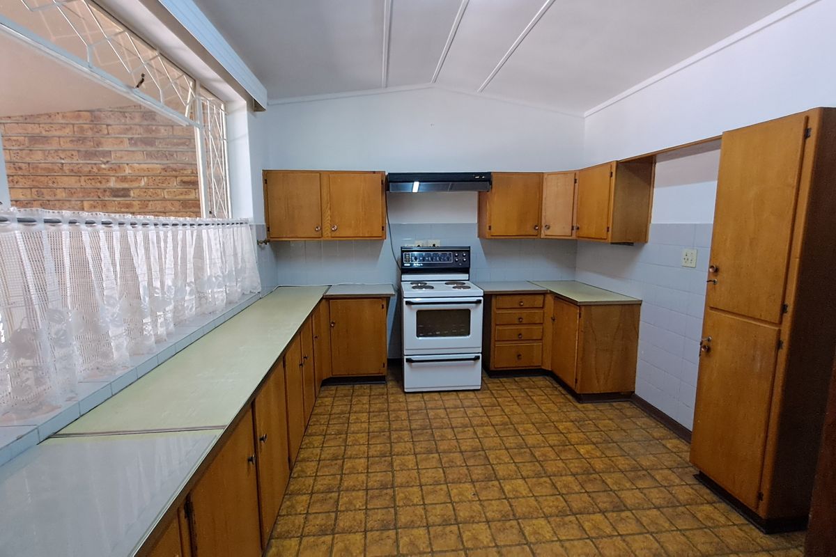 A functional kitchen featuring original wooden cabinetry, a freestanding stove with extractor fan, tiled splashbacks, and durable tiled flooring.